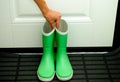 Person hand picking up pair of green child rubber boots indoors