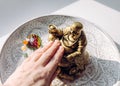 Person hand rubbing small golden laughing Buddha figurine tummy.