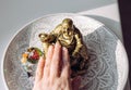 Person hand rubbing small golden laughing Buddha figurine tummy.