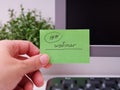 A person hand sticking a green paper note with the reminder Webinar 19-00 on it on to a monitor at office workplace Royalty Free Stock Photo