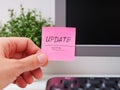 Person hand sticking a pink paper notes with the reminder Update on to a monitor at an office workplace Royalty Free Stock Photo