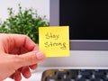 A Person hand sticking a yellow paper notes with the reminder Stay Strong on it on to a monitor at an office workplace Royalty Free Stock Photo