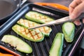 Person hand with tweezers frying organic zucchini on grill iron pan. Close-up grilled sliced vegetables cooking process for vegan