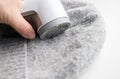 Person hand using sheaving lint balls from winter hat with lint shaver machine tool.