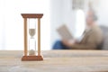 Person having some free time reading a book. An old hourglass on a wooden white table.