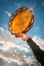 Person holding aloft a tambourine against blue sky