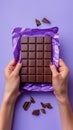 A person is holding a bar of chocolate on its wrapper in their hands, showcasing the delicious treat up close