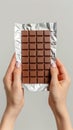 A person is holding a bar of chocolate on a silver wrapper in their hands, showcasing the delicious treat up close