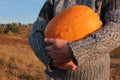 A person holding big orange pumpkin on the bright blue sky and field background. Female hands in gray sweater with huge pumpkin. C Royalty Free Stock Photo