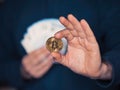 Person holding bitcoin in one hand, pile of cash money in other hand. Invest into virtual currency concept. Selective focus. Dark
