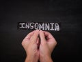 A person holding a black piece of paper with the word Insomnia on it in his hands