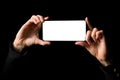 Person holding in both hands mobile phone horizontally with blank white screen, isolated on black background