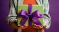 Person holding a bright green gift box with purple ribbon against a purple background Royalty Free Stock Photo