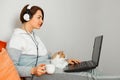 A person holding a cat and laptop. a home schooling and work at home. A woman in white headphones, in home clothes with