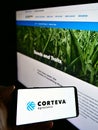 Person holding cellphone with business logo of US agricultural chemical company Corteva Inc. on screen in front of website.