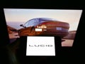 Person holding cellphone with business logo of US electric vehicle company Lucid Motors Inc. on screen in front of webpage.