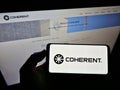 Person holding cellphone with business logo of US laser manufacturer Coherent Inc. on screen in front of company website.