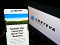 Person holding cellphone with business website of US agricultural chemical company Corteva Inc on screen with logo.