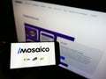 Person holding cellphone with company logo of Brazilian e-commerce platform Mosaico Tecnologia on screen in front of website.
