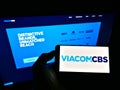 Person holding cellphone with company logo of US mass media company ViacomCBS Inc. on screen in front of business website.