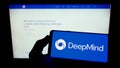 Person holding cellphone with logo of AI company DeepMind Technologies Limited on screen in front of business webpage.