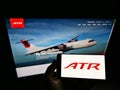 Person holding cellphone with logo of aircraft manufacturer Avions de Transport RÃÂ©gional (ATR) on screen with web page.