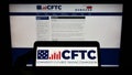 Person holding cellphone with logo of American Commodity Futures Trading Commission (CFTC) on screen with webpage.