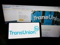 Person holding cellphone with logo of American credit reporting agency TransUnion on screen in front of business webpage.