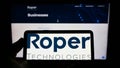 Person holding cellphone with logo of American engineering company Roper Technologies Inc. on screen in front of webpage. Royalty Free Stock Photo