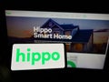 Person holding cellphone with logo of American insurance company Hippo Holdings Inc. on screen in front of webpage.