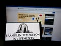 Person holding cellphone with logo of American investment firm Franklin Templeton Investments on screen in front of webpage.