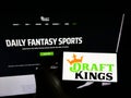 Person holding cellphone with logo of American sports betting company DraftKings Inc. on screen in front of webpage.