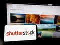 Person holding cellphone with logo of American stock photography company Shutterstock Inc. on screen in front of webpage.