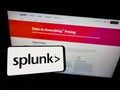 Person holding cellphone with logo of American technology company Splunk Inc. on screen in front of business webpage.