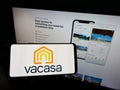 Person holding cellphone with logo of American vacation rental company Vacasa LLC on screen in front of business webpage.