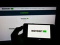 Person holding cellphone with logo of Australian battery company Novonix Limited on screen in front of business webpage.