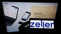 Person holding cellphone with logo of Australian fintech company Zeller (myzeller) on screen in front of webpage.