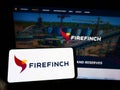 Person holding cellphone with logo of Australian gold mining company Firefinch Limited on screen in front of webpage.