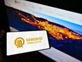 Person holding cellphone with logo of Australian gold mining company Newcrest Mining Limited on screen in front of webpage.