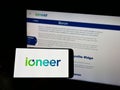 Person holding cellphone with logo of Australian mining company company ioneer Ltd. on screen in front of webpage.