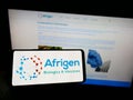 Person holding cellphone with logo of biotechnology company Afrigen Biologics Pty. Ltd. on screen in front of webpage.