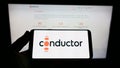 Person holding cellphone with logo of Brazilian payment company Conductor Technology Ltd. on screen in front of webpage.