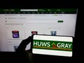 Person holding cellphone with logo of British builders merchant company Huws Gray Limited on screen in front of web page.