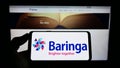 Person holding cellphone with logo of British consulting company Baringa Partners LLP on screen in front of webpage.