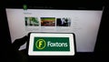 Person holding cellphone with logo of British estate agency Foxtons Group plc on screen in front of business webpage.