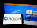 Person holding cellphone with logo of British event management company Hopin Ltd. on screen in front of business webpage.