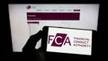 Person holding cellphone with logo of British Financial Conduct Authority (FCA) on screen in front of webpage. Royalty Free Stock Photo