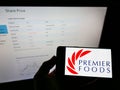 Person holding cellphone with logo of British food manufacturer Premier Foods plc on screen in front of business web page.