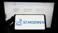 Person holding cellphone with logo of British property company St. Modwen Properties plc on screen in front of webpage.