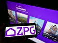 Person holding cellphone with logo of British real estate company ZPG Limited on screen in front of business webpage.